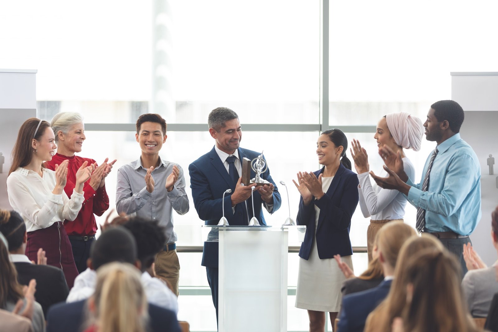 businessman holding award on podium with colleagues at business seminar